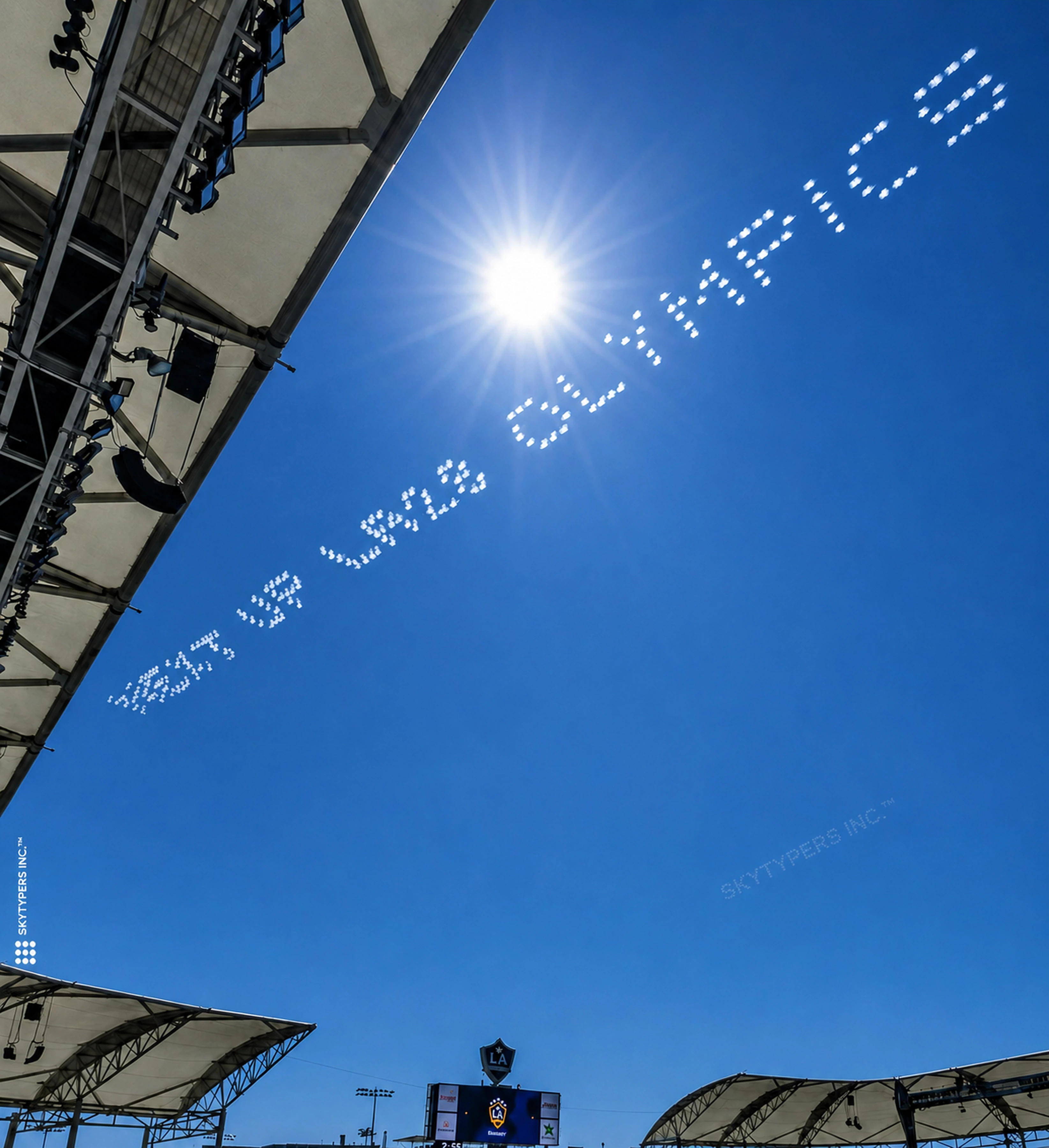White dotted skytyping across a blue sky over a Los Angeles stadium, from the Skytypers campaign archive