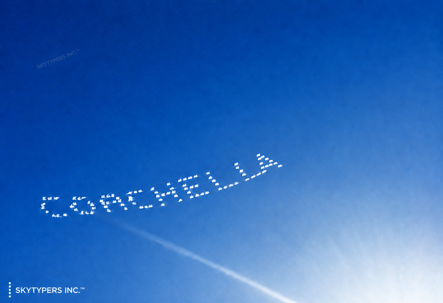 COACHELLA written in white smoke dots across the blue sky, with the Skytypers Inc. watermark