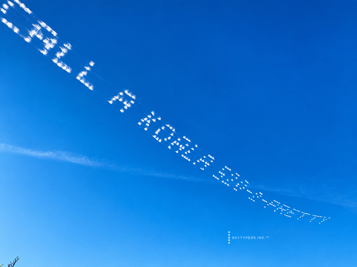 A long white skytyped message receding diagonally across blue sky, with its beginning partly outside the frame.