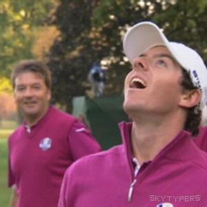 A person in a white cap and magenta golf shirt looks upward, with another golfer and trees behind them.