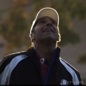 A person wearing a cap and dark sports jacket looks up in warm outdoor light.
