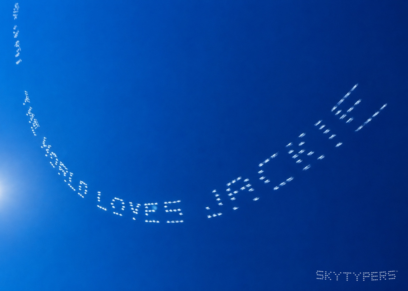 THE WORLD LOVES JACKIE in white skytyping across a blue sky.