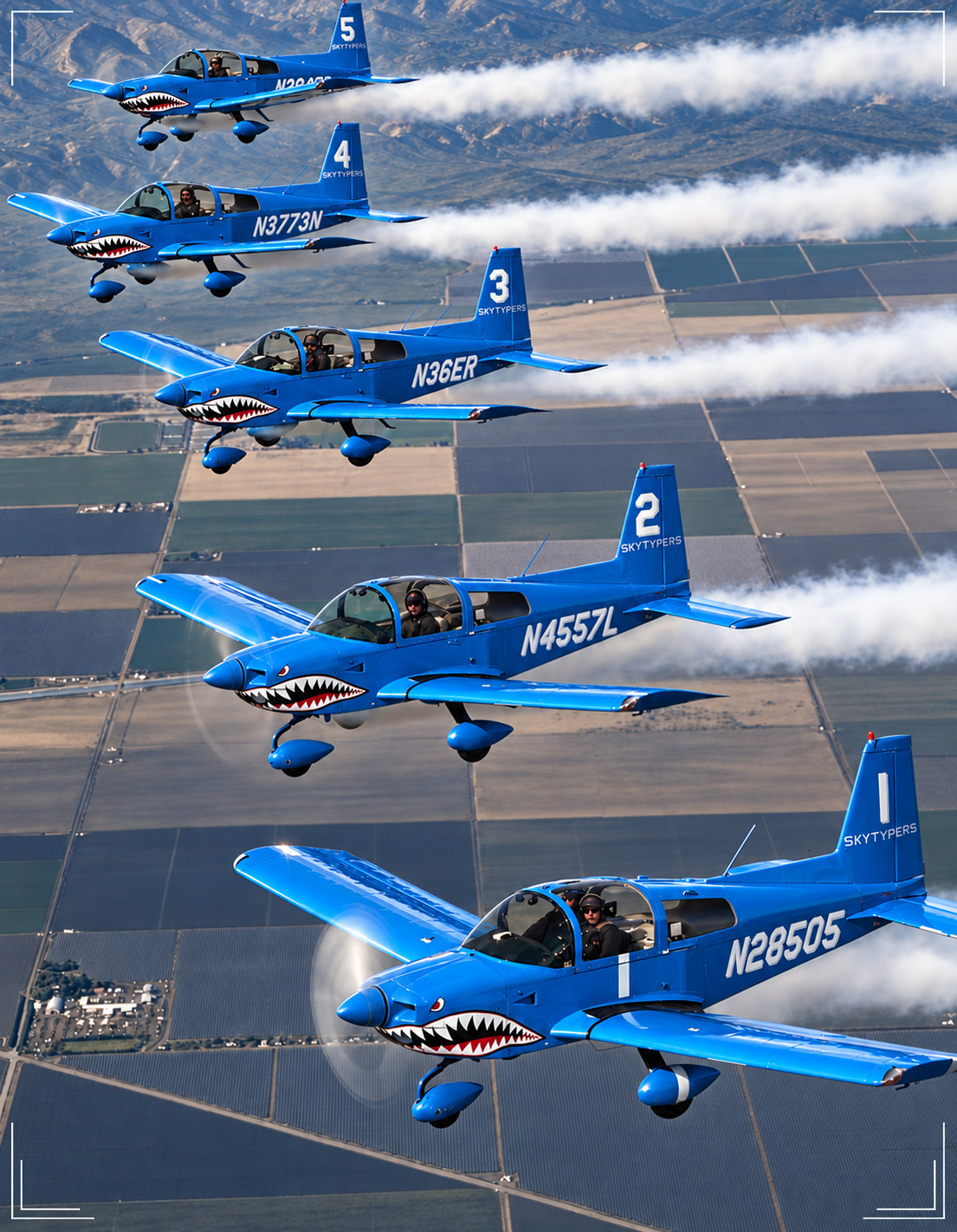 Five blue Skytypers aircraft in formation, leaving white smoke over fields.
