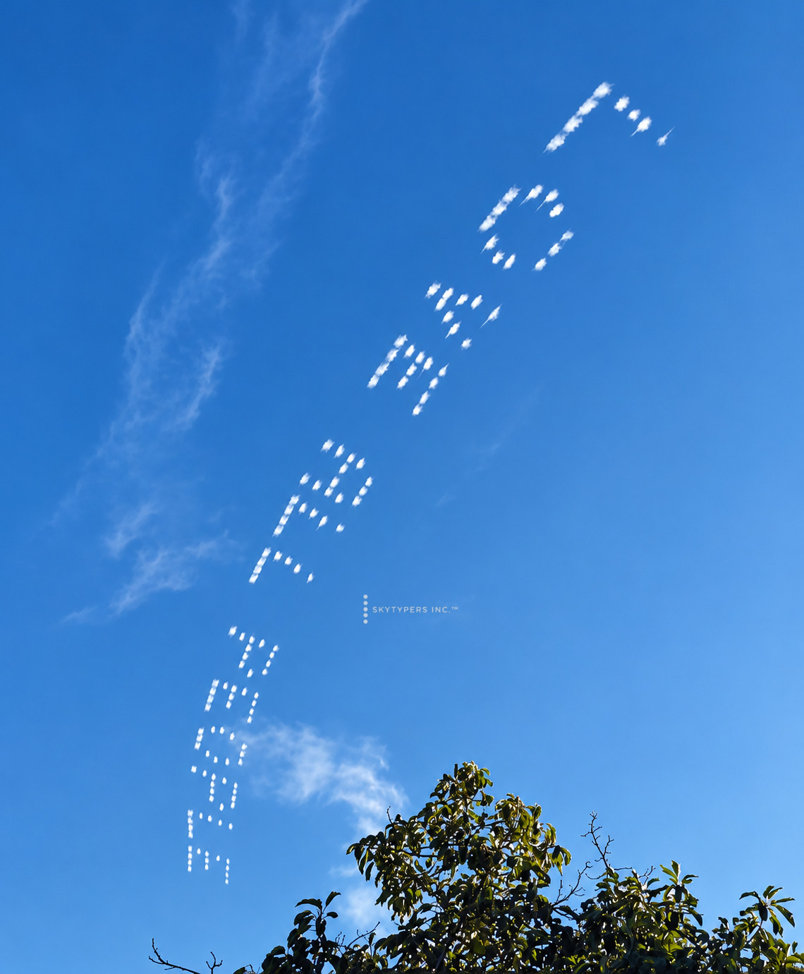 LOVE ALL PEOPLE written in white smoke above trees.