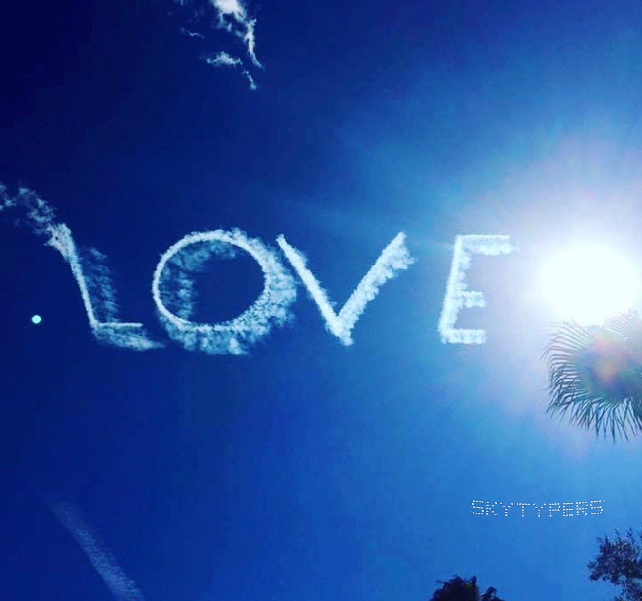 The word LOVE formed from flowing white smoke against a deep blue sky.