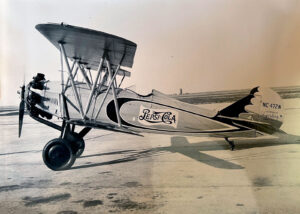 A vintage biplane with "Pepsi-Cola" branding on the fuselage, parked on a tarmac.