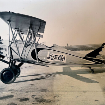 A vintage biplane with "Pepsi-Cola" branding on the fuselage, parked on a tarmac.