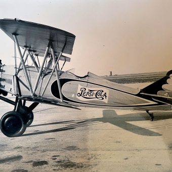 A vintage biplane with "Pepsi-Cola" branding on the fuselage, parked on a tarmac.